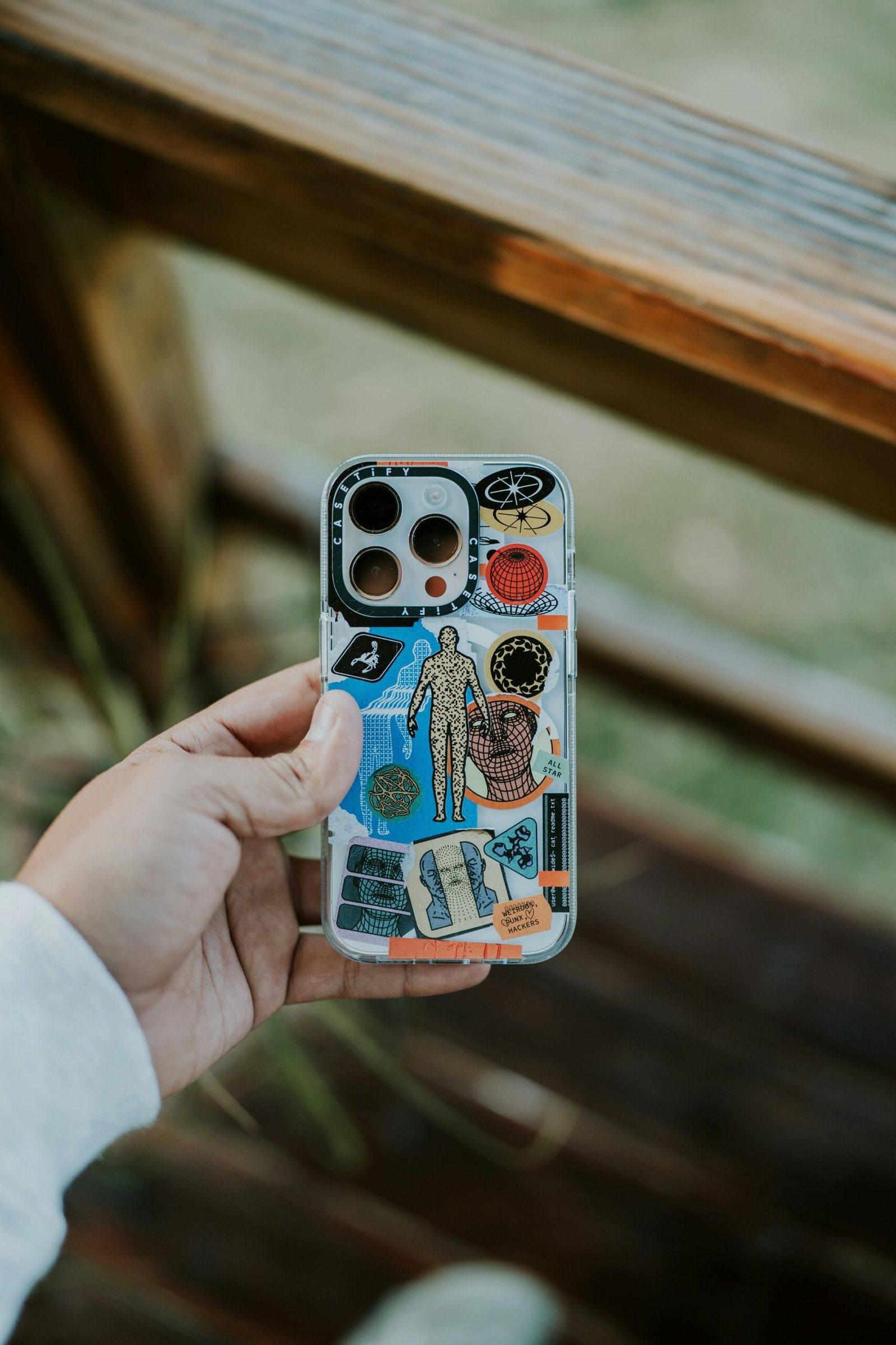 A close-up of a hand holding a creatively designed smartphone case outdoors, featuring various colorful elements.