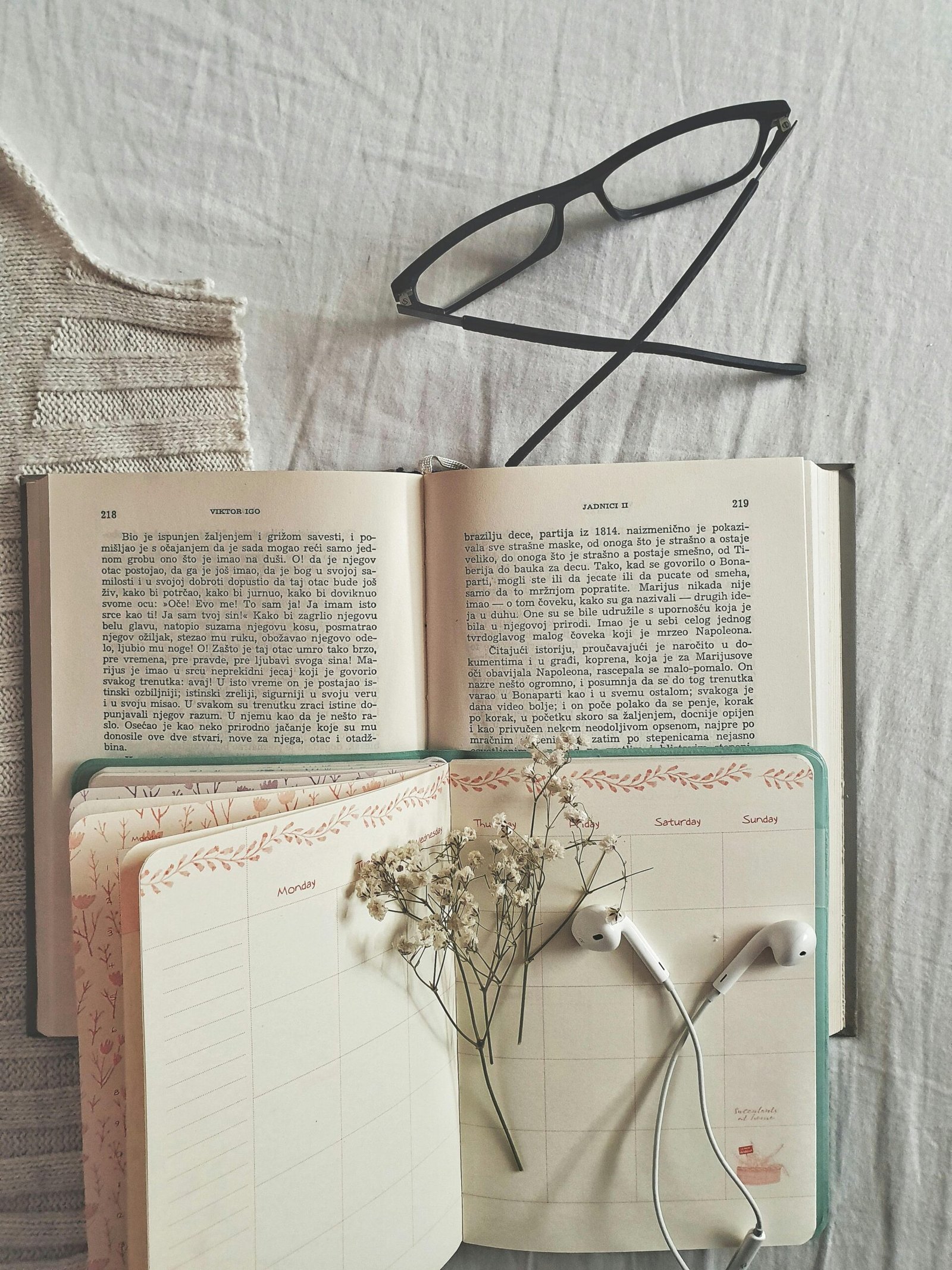 Flat lay of an open book, planner, and eyeglasses creating a cozy and intellectual setting.